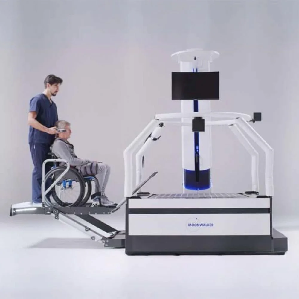 A person in a wheelchair is being assisted onto a robotic device labeled 'MOONWALKER' with a large robotic arm and a display screen, likely for medical or rehabilitation purposes.