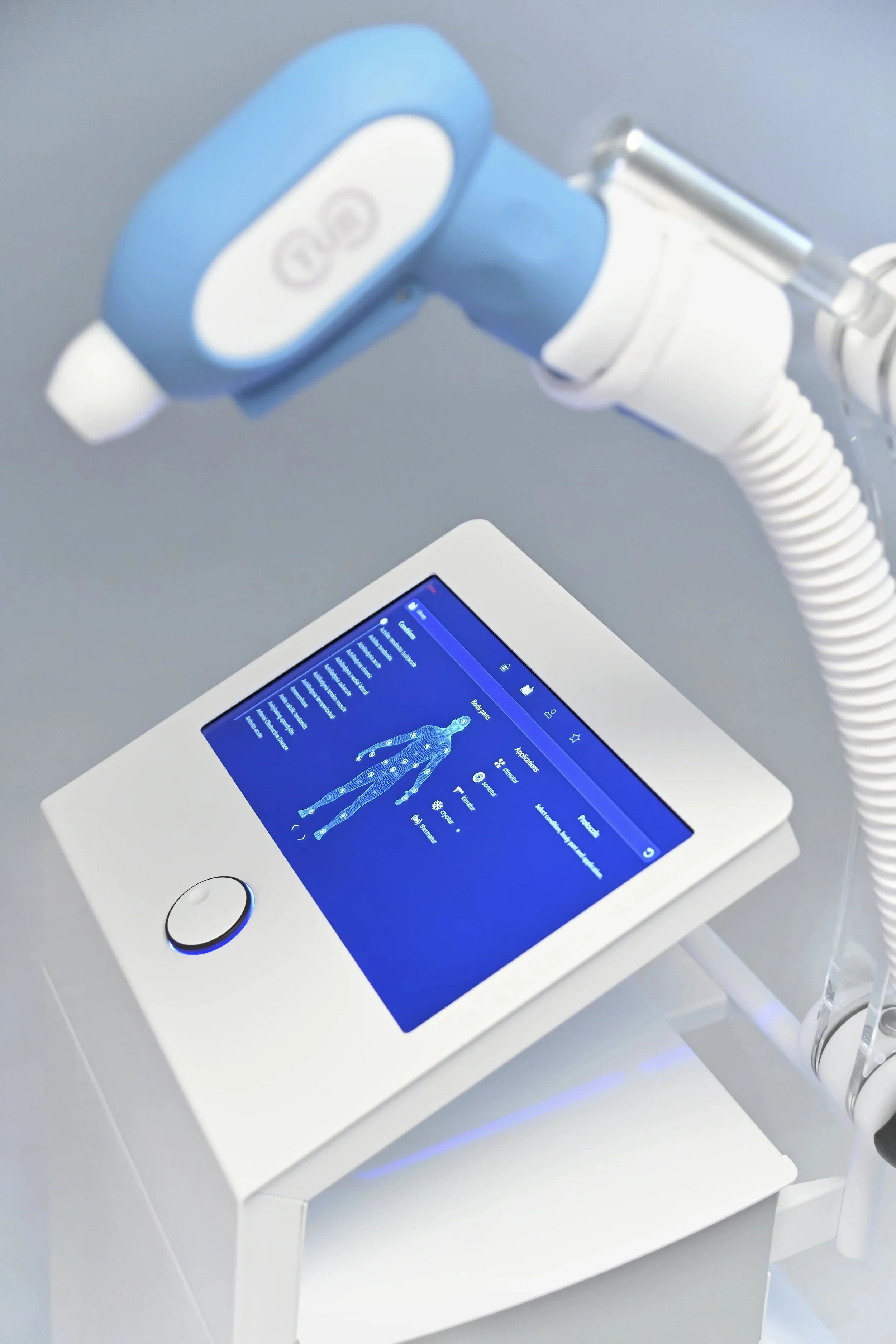 Medical device on a white stand connected to a tablet showing a digital human body interface.