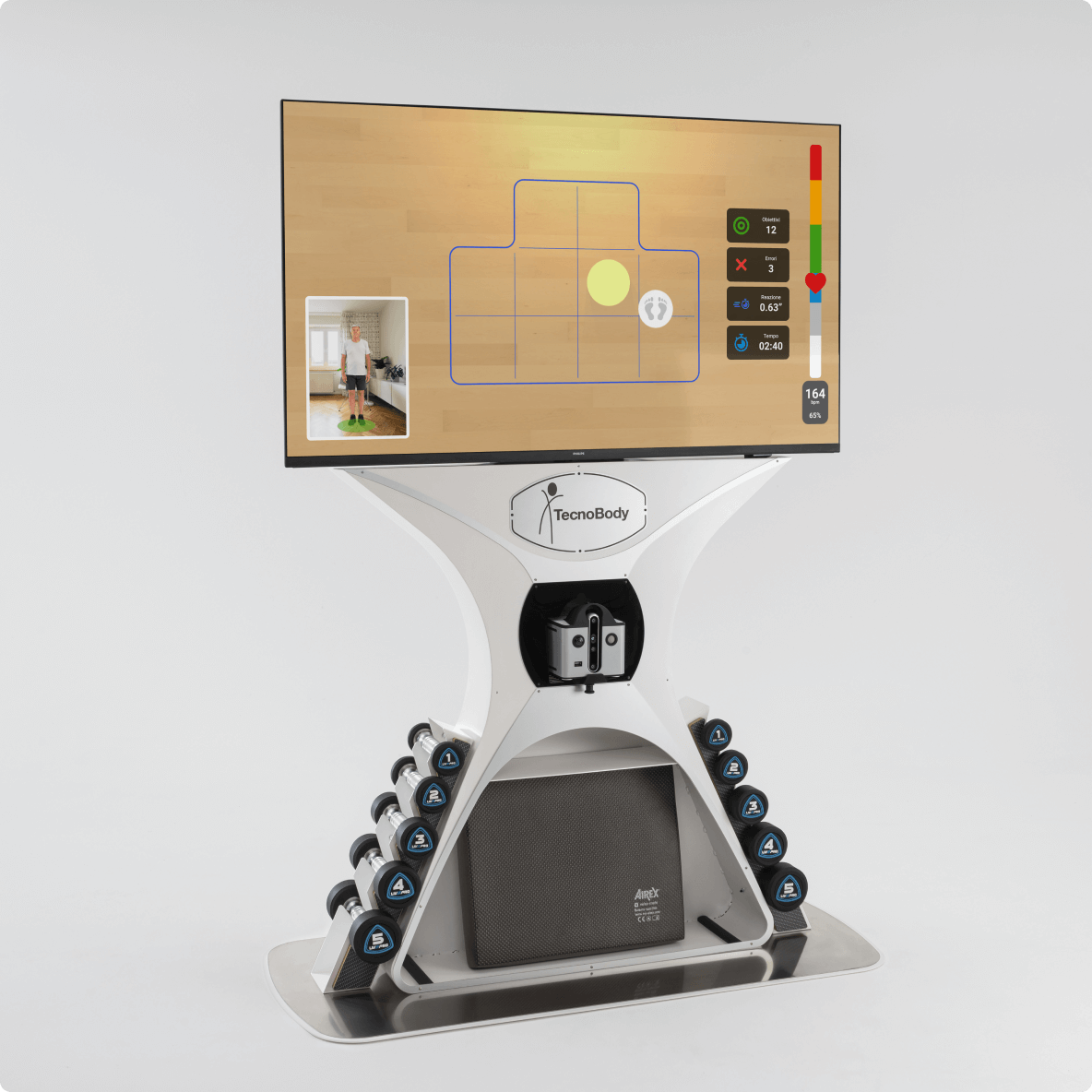 A TecnoBody fitness machine with a large digital screen, a set of weight sensors, and a person standing on a green sensor pad. The screen displays a tennis court layout, exercise metrics, and a small video feed of the person. The machine has numbered weight stations on either side.