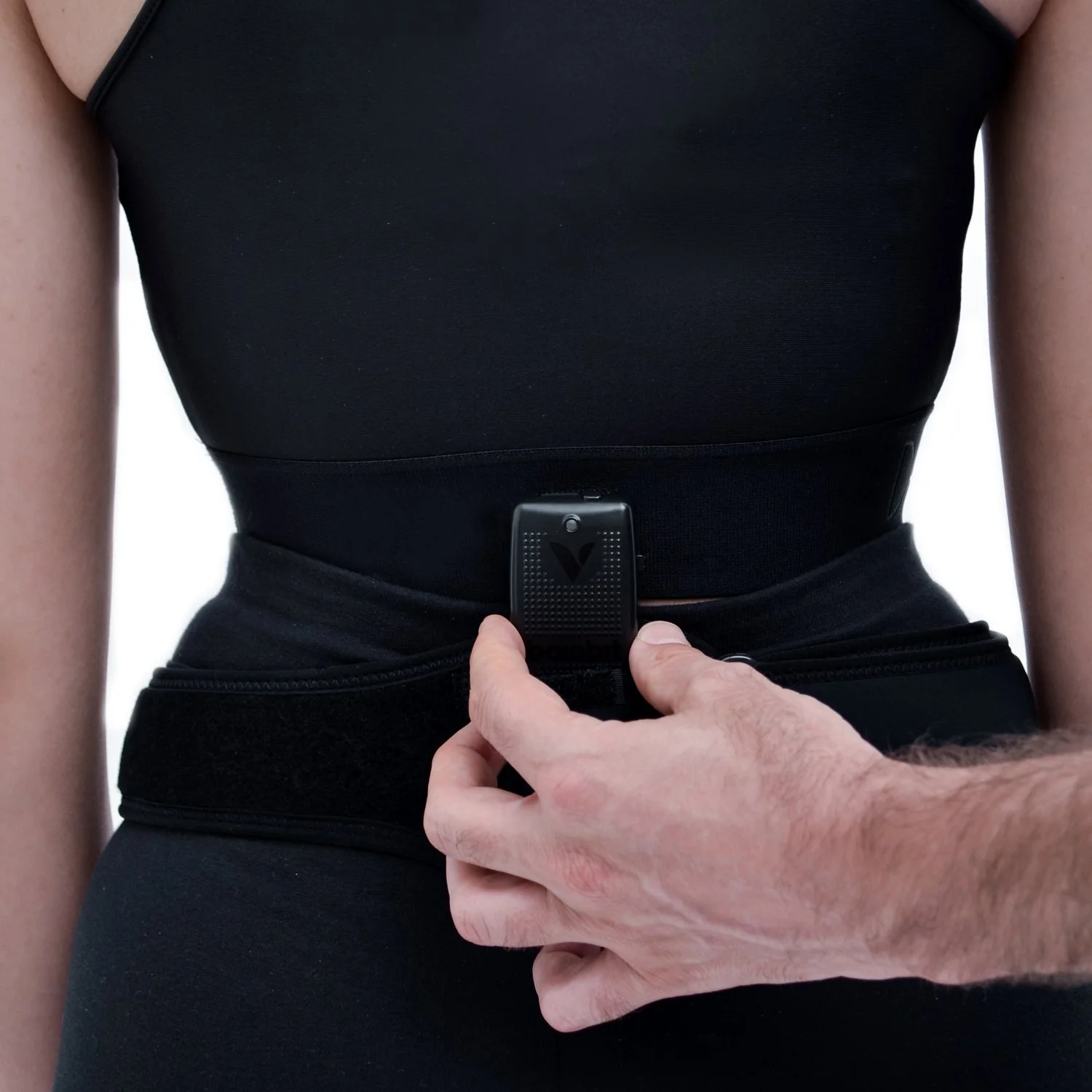 Close-up of a person wearing a black fitness vest and pants, with a fitness tracker on the waist, as another person adjusts the tracker.