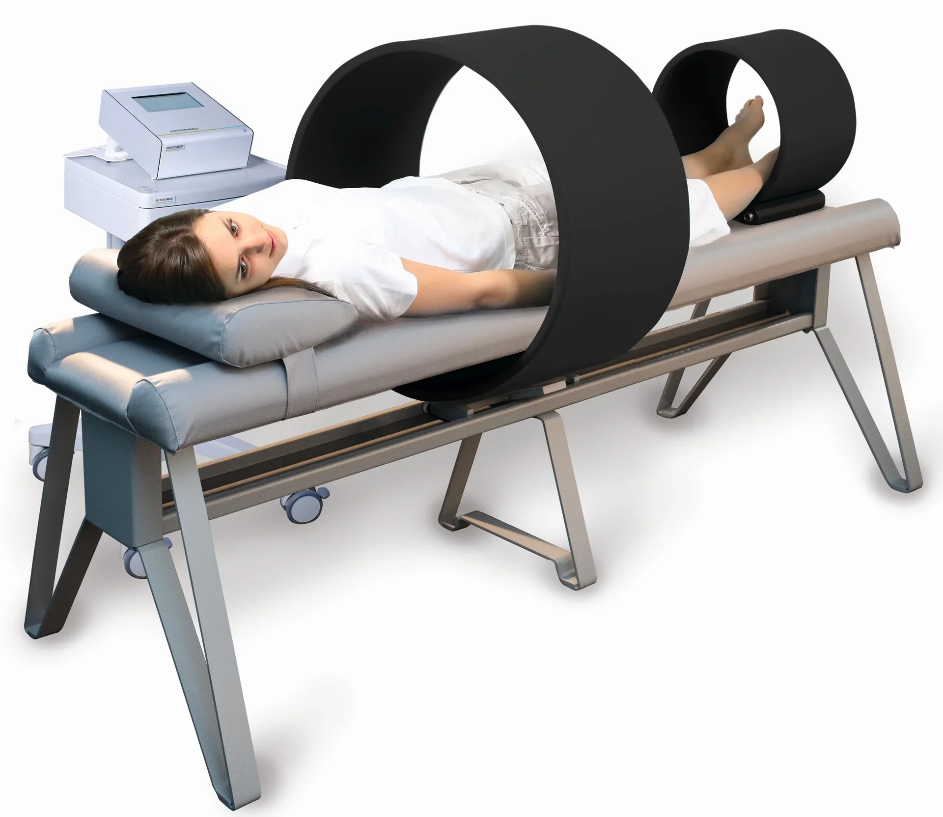 A woman lying on a medical examination table with a black CT scanner partially surrounding her legs for imaging.