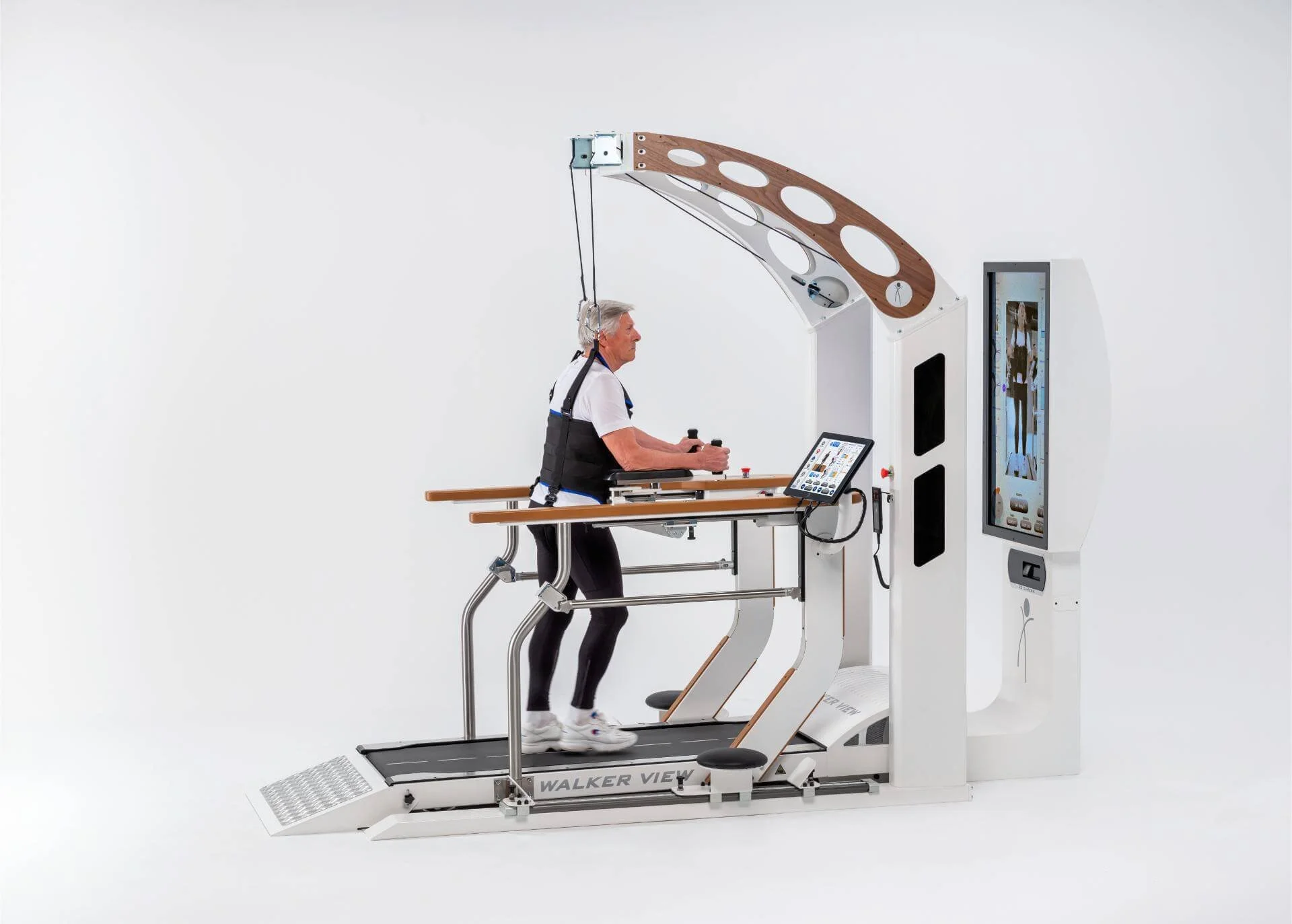 Elderly man walking on a gait training machine with a harness and safety rails in a clinical setting.