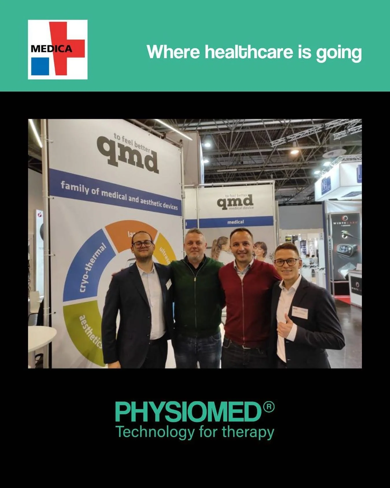 Four men standing together at a healthcare technology expo, smiling and posing for a photo in front of medical display banners and signs. The background features expo booths and lighting.
