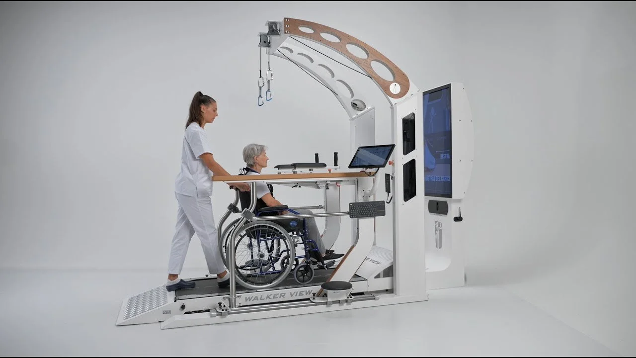 A medical robotic system assisting a healthcare worker and a patient in a wheelchair, featuring a touchscreen interface and a mechanical lifting arm.