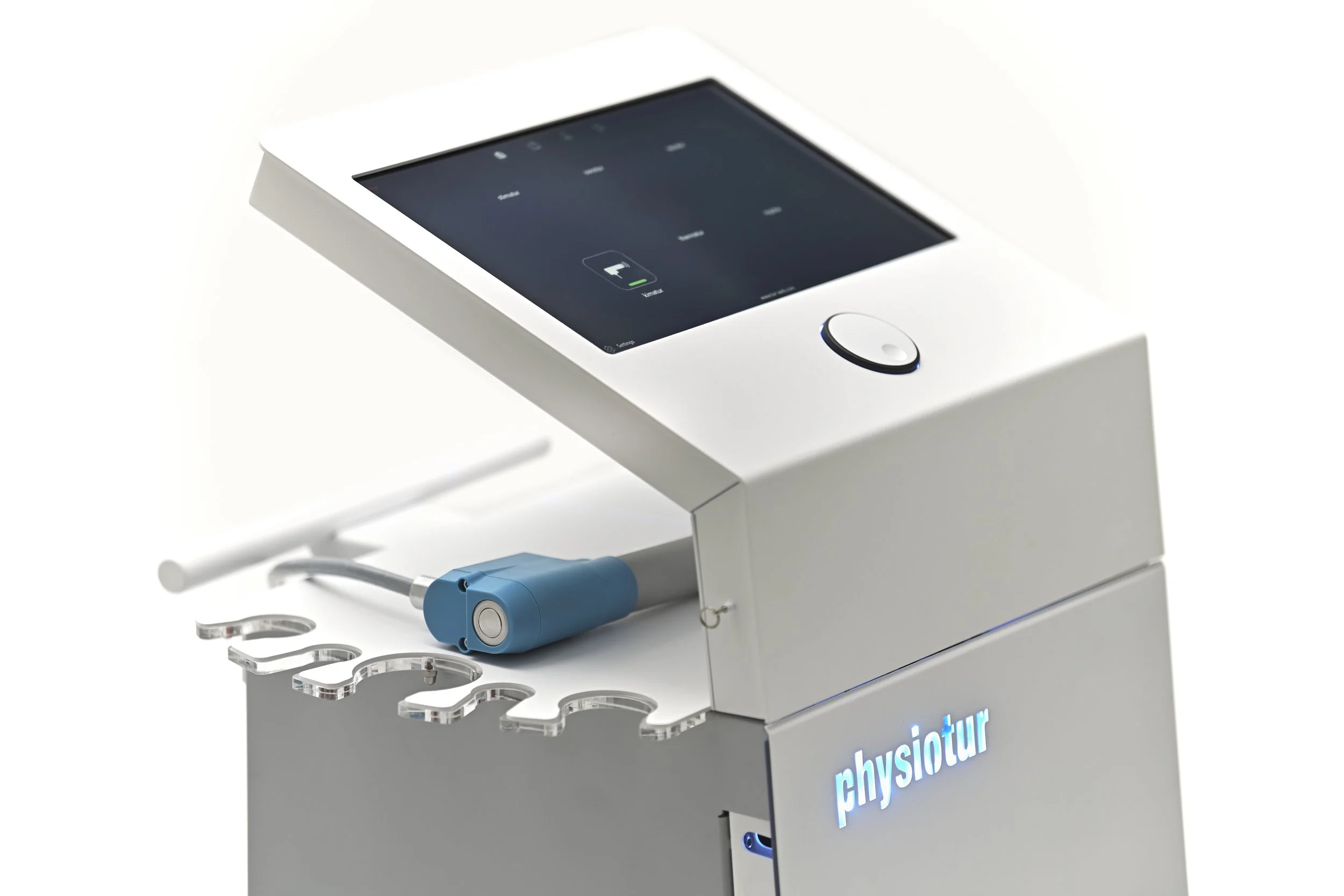 A modern medical device with a touchscreen display, labeled 'physiotur', connected to a blue handheld tool with a cable, positioned above a white stand with multiple cutouts.