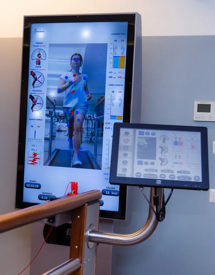A person is running on a treadmill with a large screen displaying body movement analysis and metrics, and a smaller control panel in front showing various controls and data.