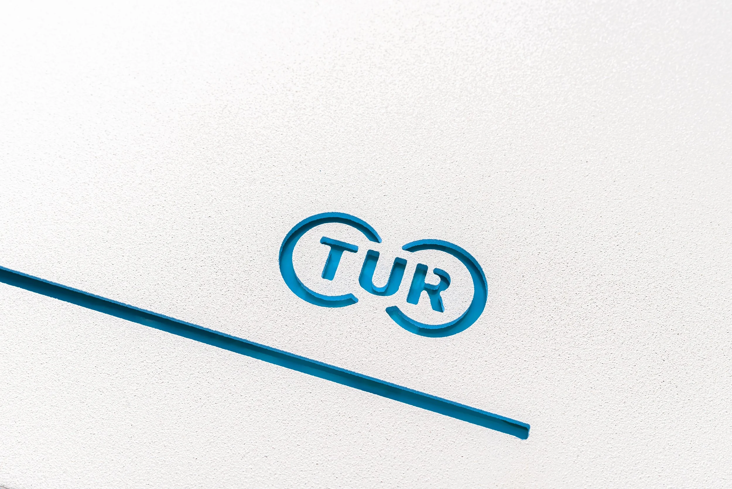 Close-up of a textured white surface with a blue logo of a company named 'Turi' embossed on it.