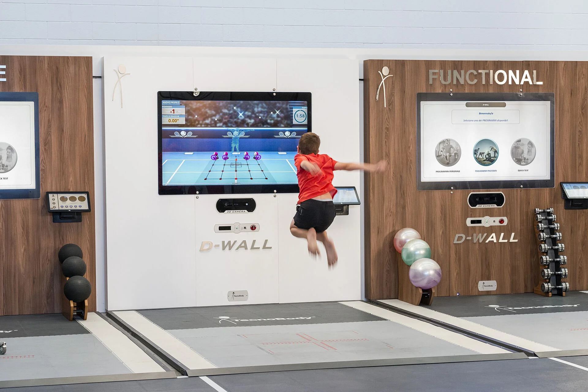 Child in red shirt and black shorts jumping on a trampoline with a digital fitness screen in the background showing a sport activity simulation.