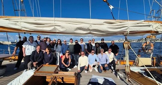 Group of people on a sailboat with blue skies and calm waters in the background