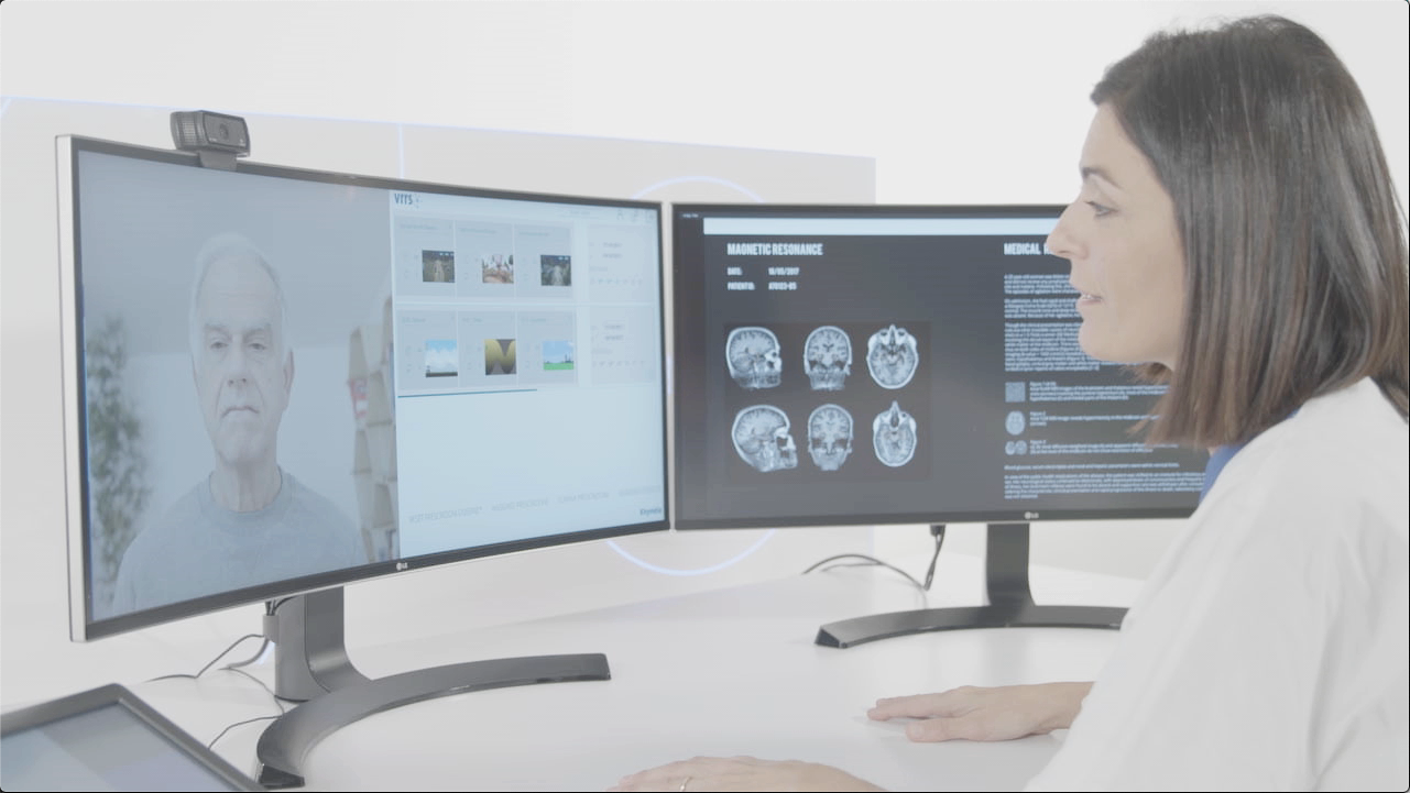 A female medical professional reviewing brain MRI scans on dual monitors while participating in a telemedicine consultation with an older man.