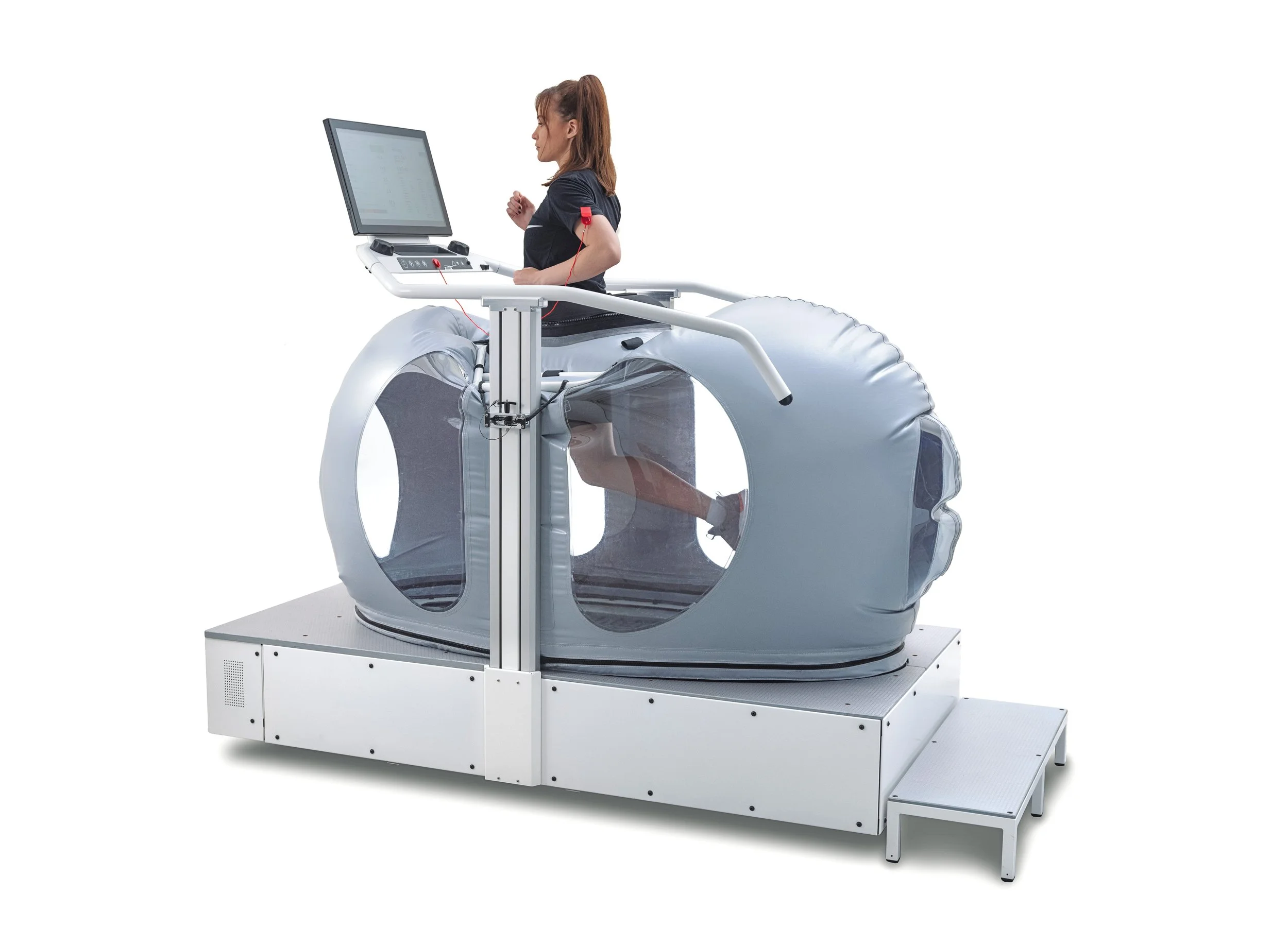 A woman undergoing a medical procedure inside a modern hyperbaric oxygen chamber with a computer monitor attached.