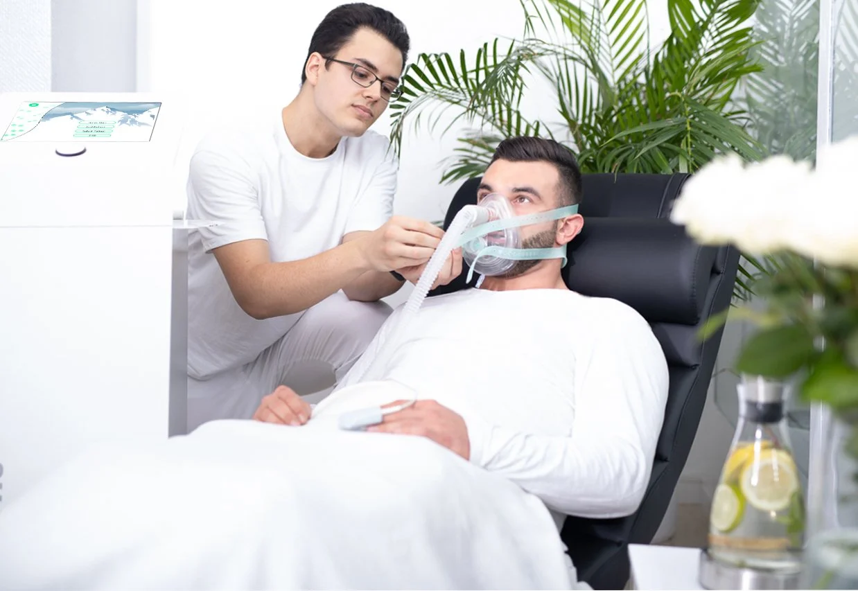 A doctor checking on a patient lying in a hospital bed with an oxygen mask, surrounded by green plants and medical equipment.
