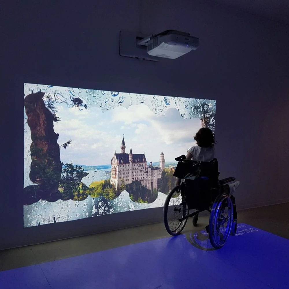 A person in a wheelchair viewing a digital projection of a castle on a wall.