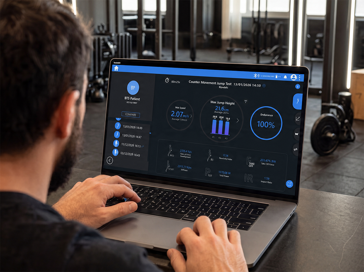 Man working on laptop in gym displaying health and performance metrics on screen.