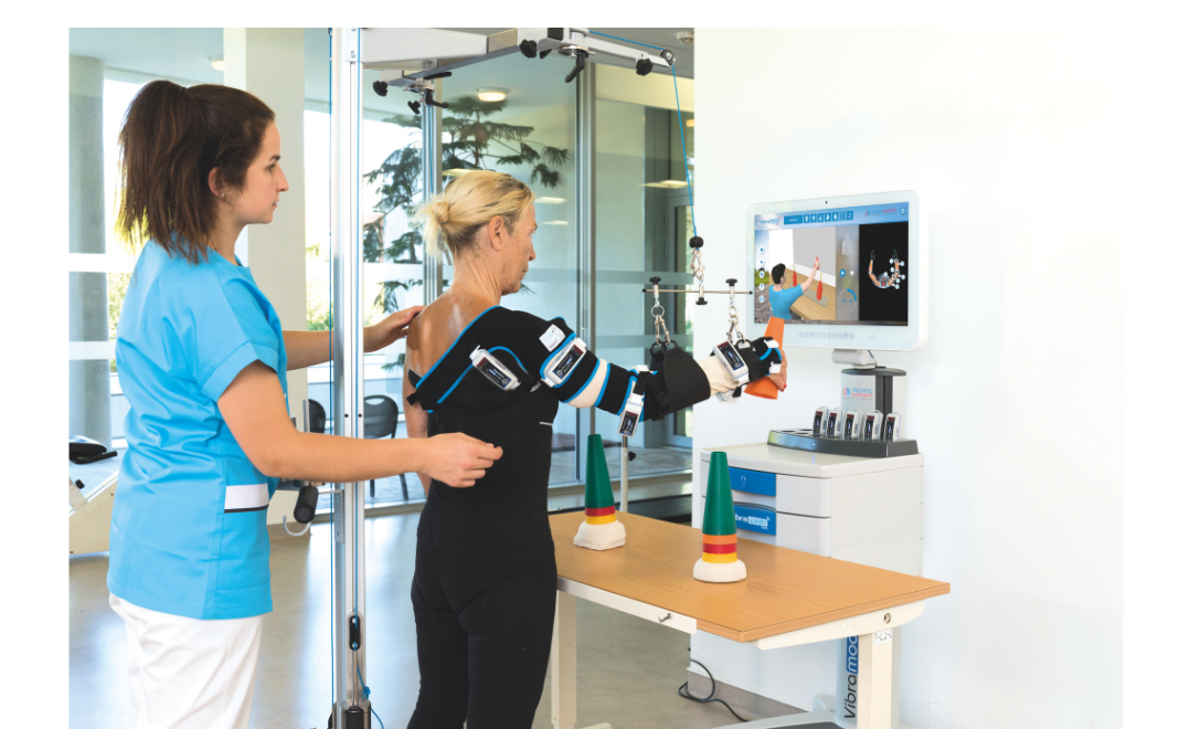 A woman undergoing occupational therapy using robotic devices to move her arms, guided by a therapist in a clinical setting.