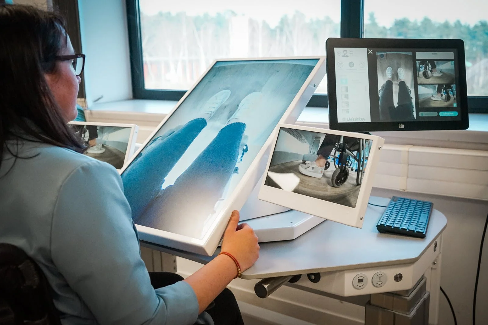 A person in a wheelchair using a virtual reality scanning device with multiple monitors showing the person's legs and feet from different angles.