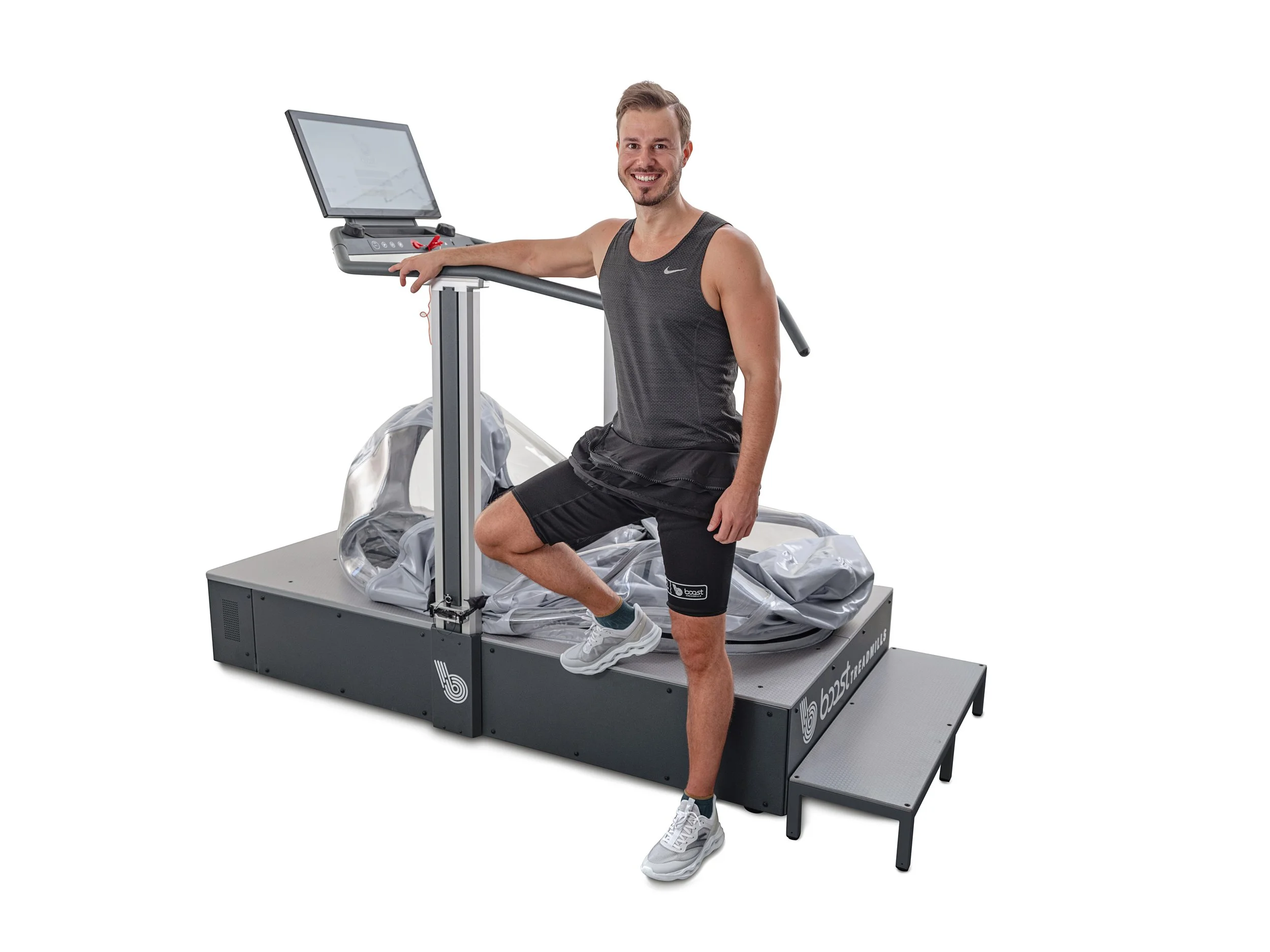 Smiling man in athletic clothing using a Treadmill BioBeam 6.0, a machine for blood flow restriction training, on white background.