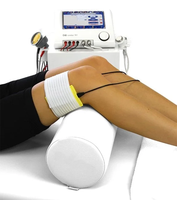 A person undergoing electrical muscle stimulation therapy on their thigh, connected via wires to a medical device with a screen.