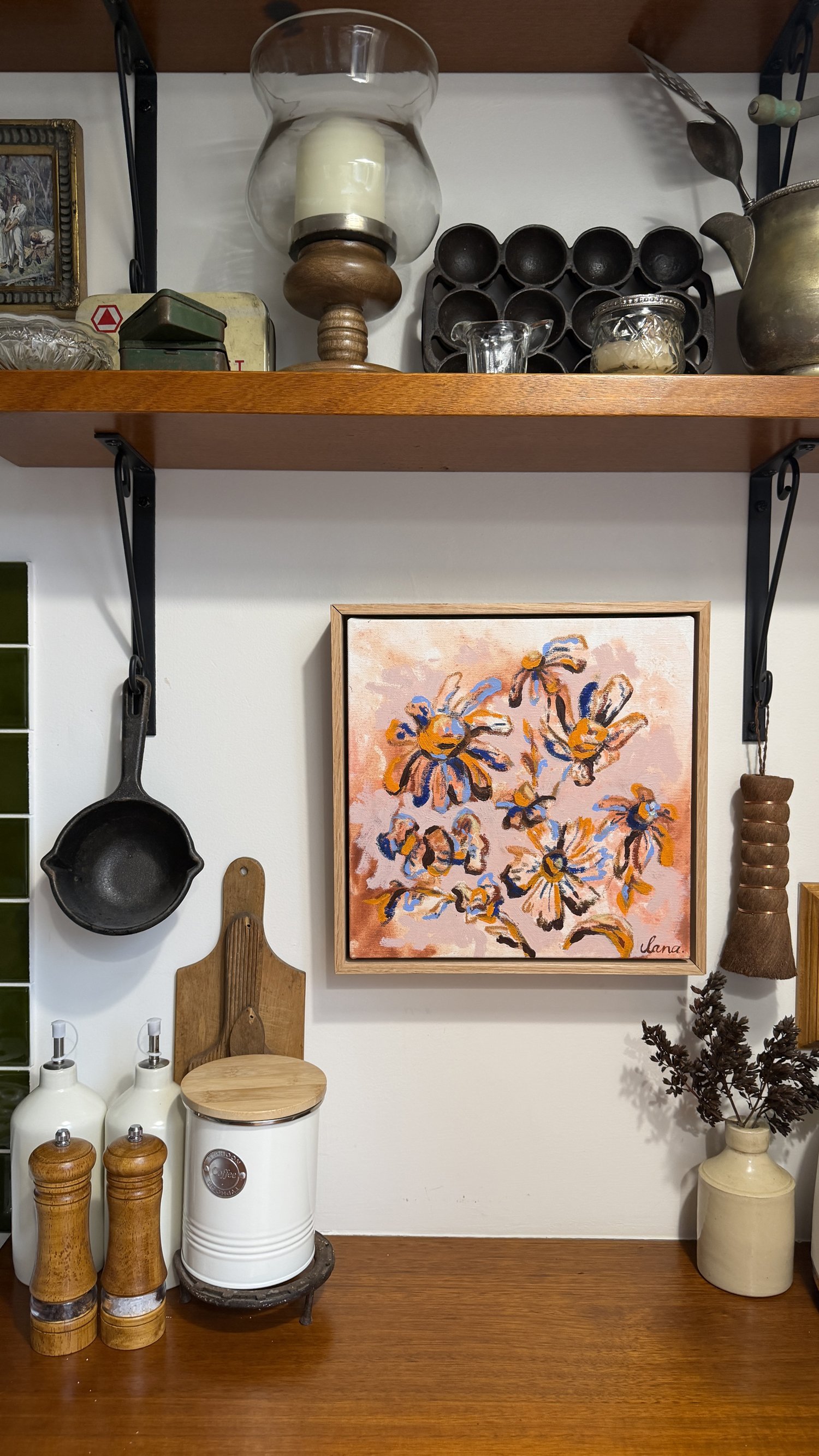Abstract floral painting with loose orange, blue and rust-toned blooms on a blush pink background, natural oak frame