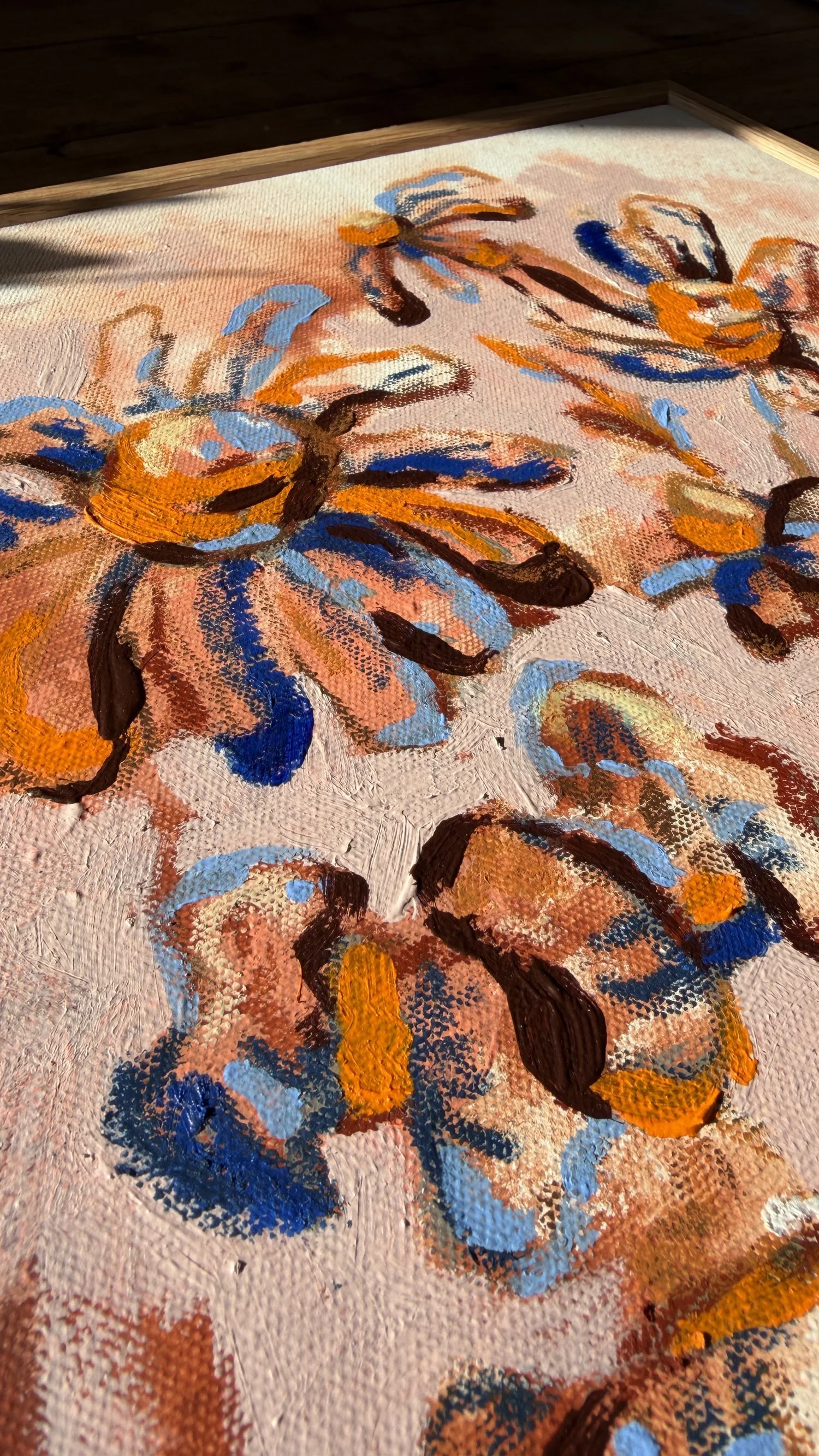 Abstract floral painting with loose orange, blue and rust-toned blooms on a blush pink background, natural oak frame