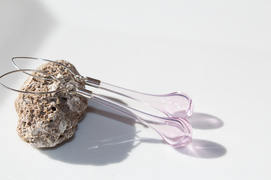 Boucles d'oreilles en verre rose reposant sur une pierre poreuse blanche avec ombres portées.