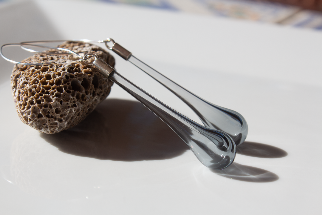 Deux ciseaux en verre posés sur une pierre poreuse sur une surface blanche, avec une lumière naturelle.
