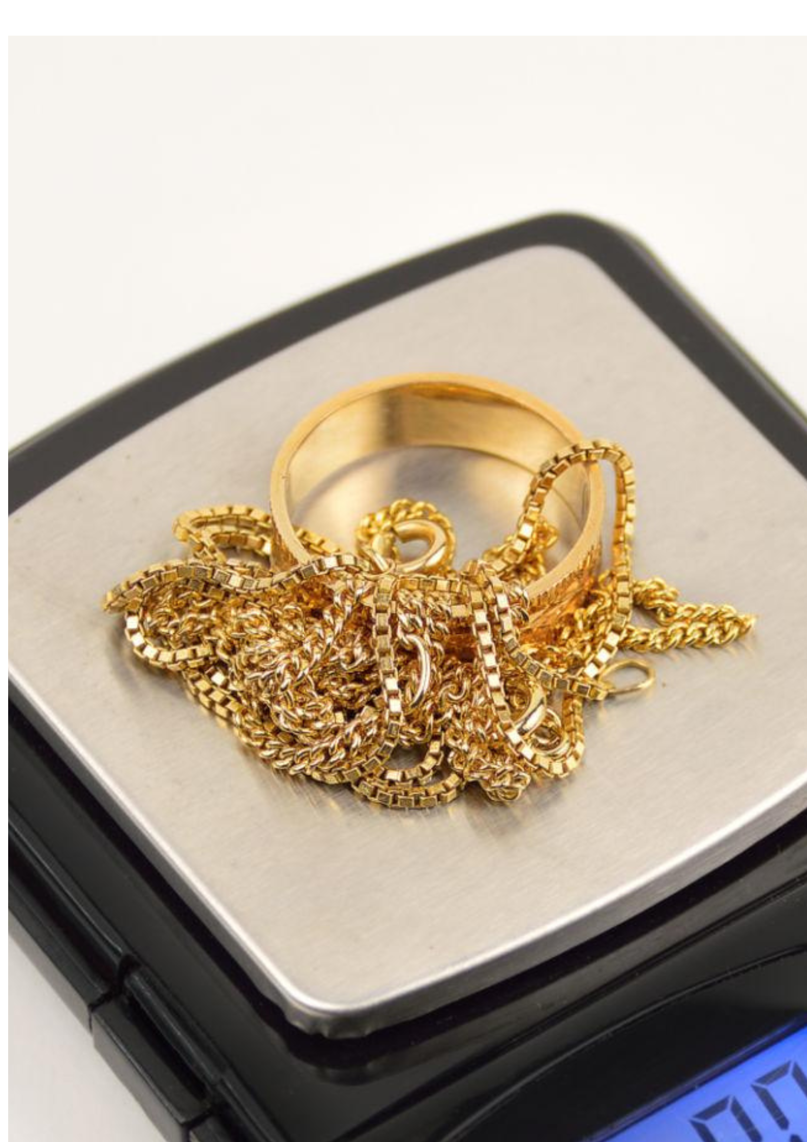 Des bijoux en or, y compris une bague et plusieurs chaînes, posés sur une balance numérique dans un écrin
