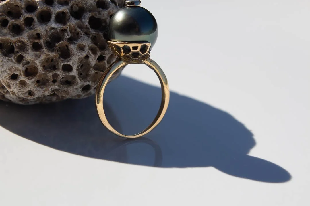 Bague en or avec une pierre noire, posée contre une roche poreuse, avec une ombre nette.