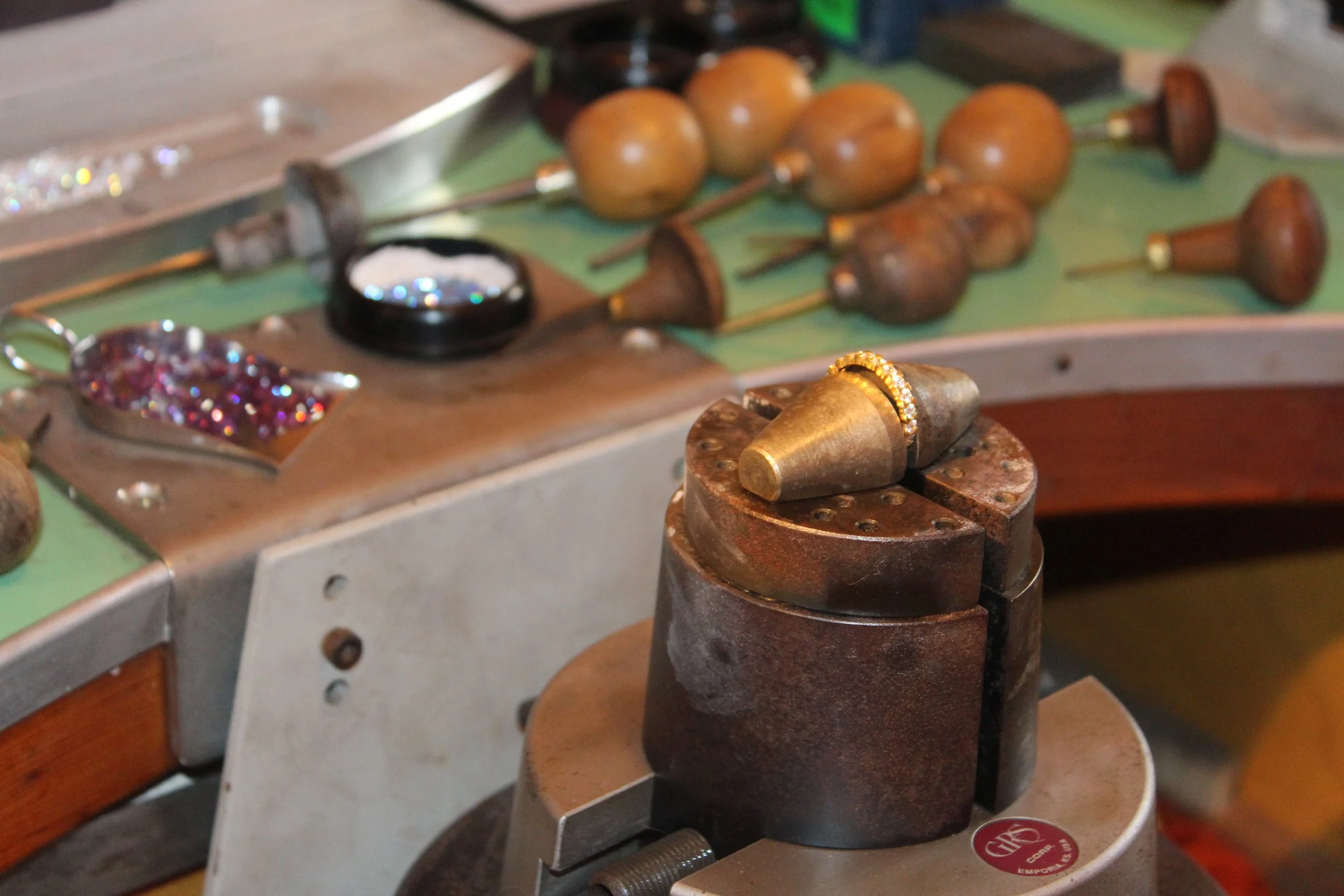 Outils de bijouterie, notamment une presse à sertir de bijoux avec plusieurs runes et pierres précieuses, et des perforateurs pour bijoux, posés sur une surface de travail.