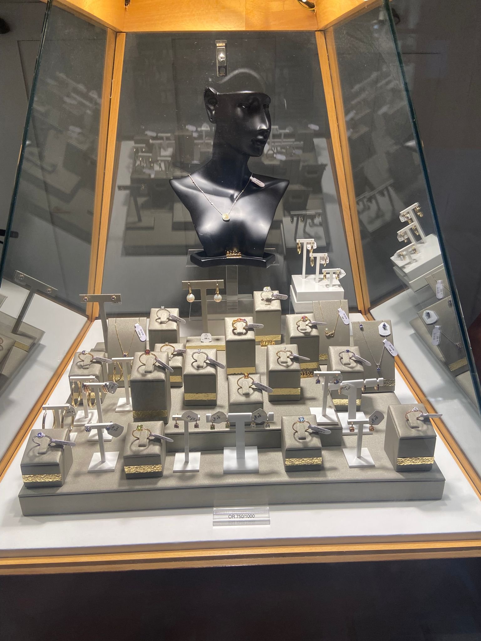 Vitrine de bijoux avec un mannequin noir portant un collier en or et diamants, et plusieurs bagues, boucles d'oreilles et colliers exposés sur des stands et supports