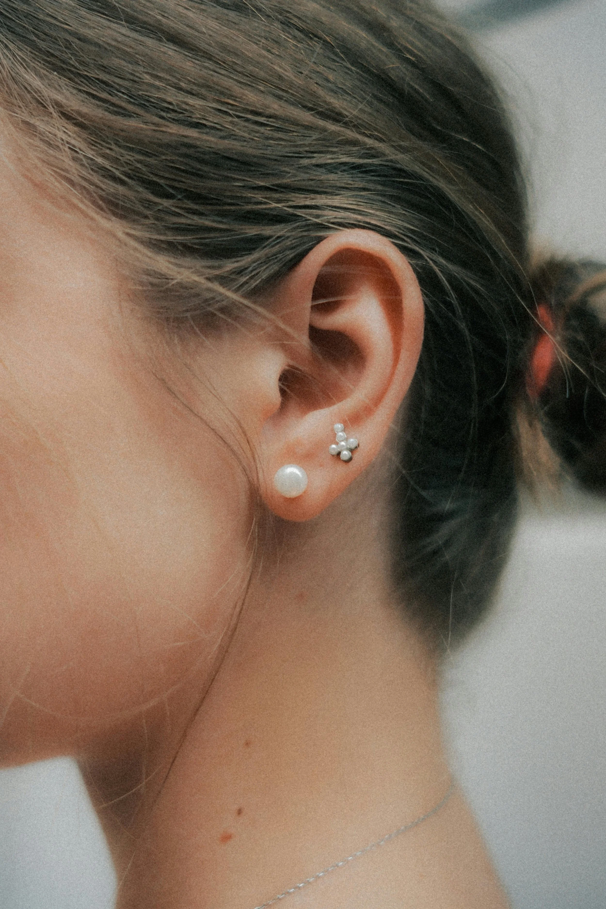 Une personne porte trois boucles d'oreilles : une perle, une petite boule en argent et une autre forme en croix avec des petites perles.
