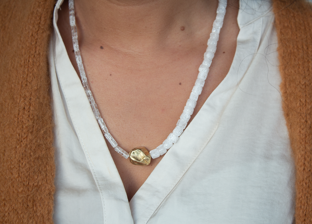 Un gros plan sur un cou avec un collier en perles blanches et une pièce en or.