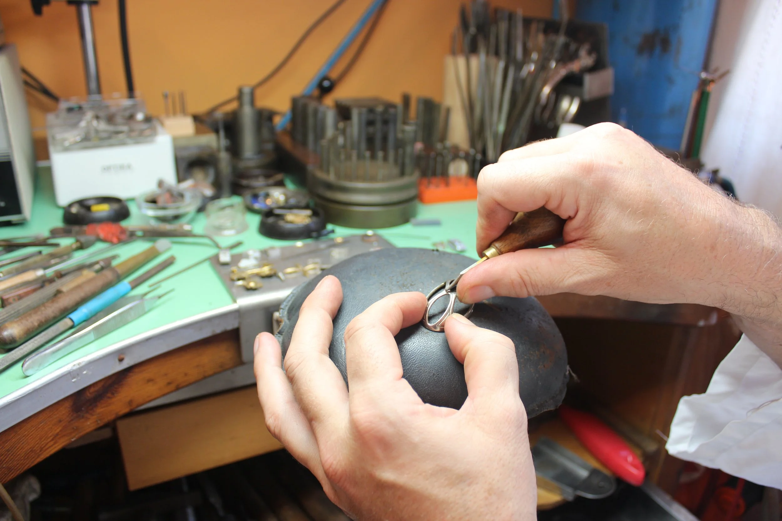 Un artisan forge et façonne un accessoire en métal à l'aide d'outils de précision sur un établi de travail.