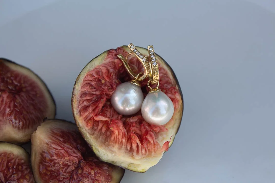 Boucles d'oreilles en or avec perles, posées sur une figue coupée.