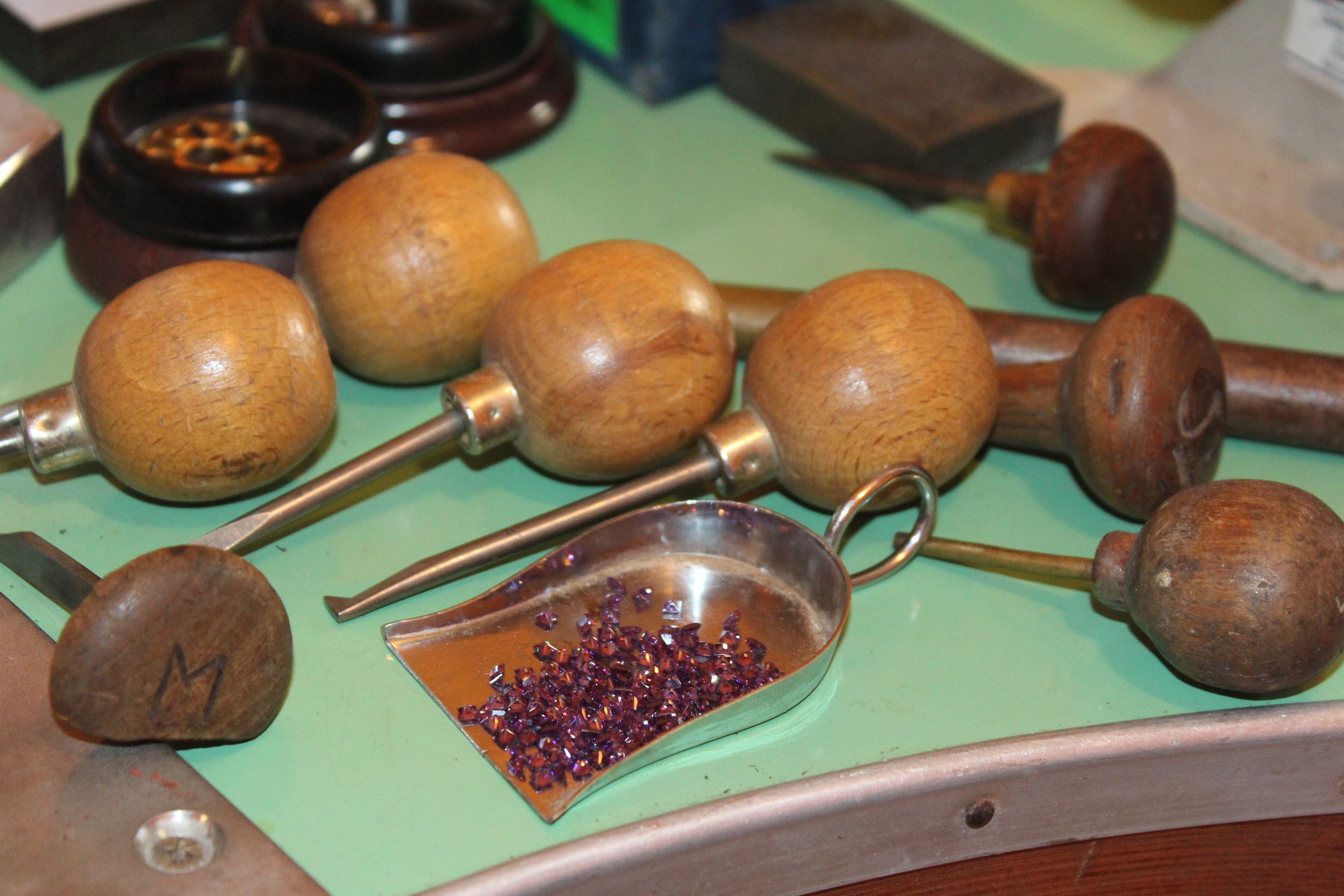 Outils en bois et métal sur une table verte, incluant des marteaux en bois, un sachet de petits cristaux violets, et d'autres éléments artisanaux.