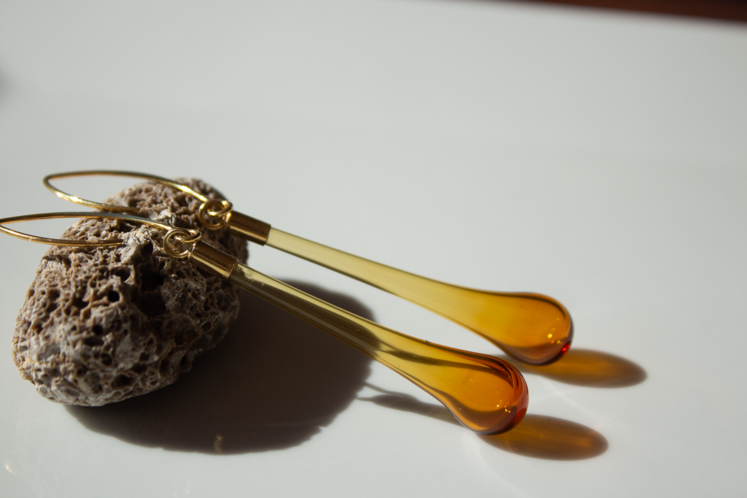 Boucles d'oreilles en verre orange et jaune posées sur une pierre volcanique, avec un éclairage créant des ombres.