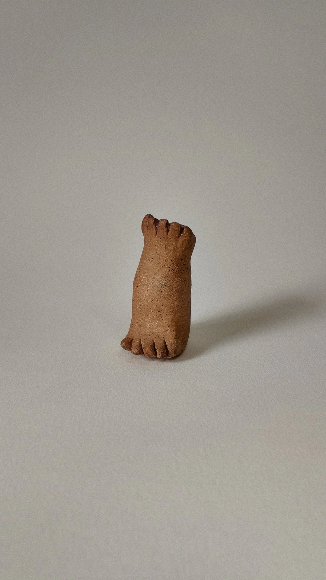 A small, brown clay figurine in the shape of a hand with fingers closed into a fist, standing on a flat surface.