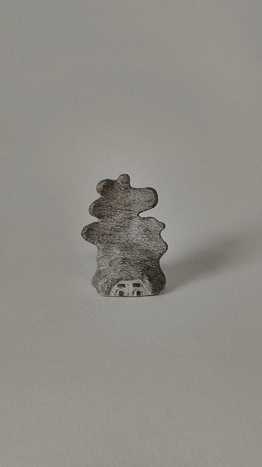 A small wooden figurine shaped like a bear, painted with a gray and white pattern, sitting on a plain, light-colored surface.