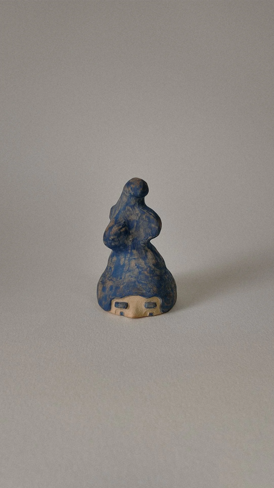 Small ceramic figurine resembling a woman with a blue dress and pied-de-poules pattern, facing forward with a neutral expression.