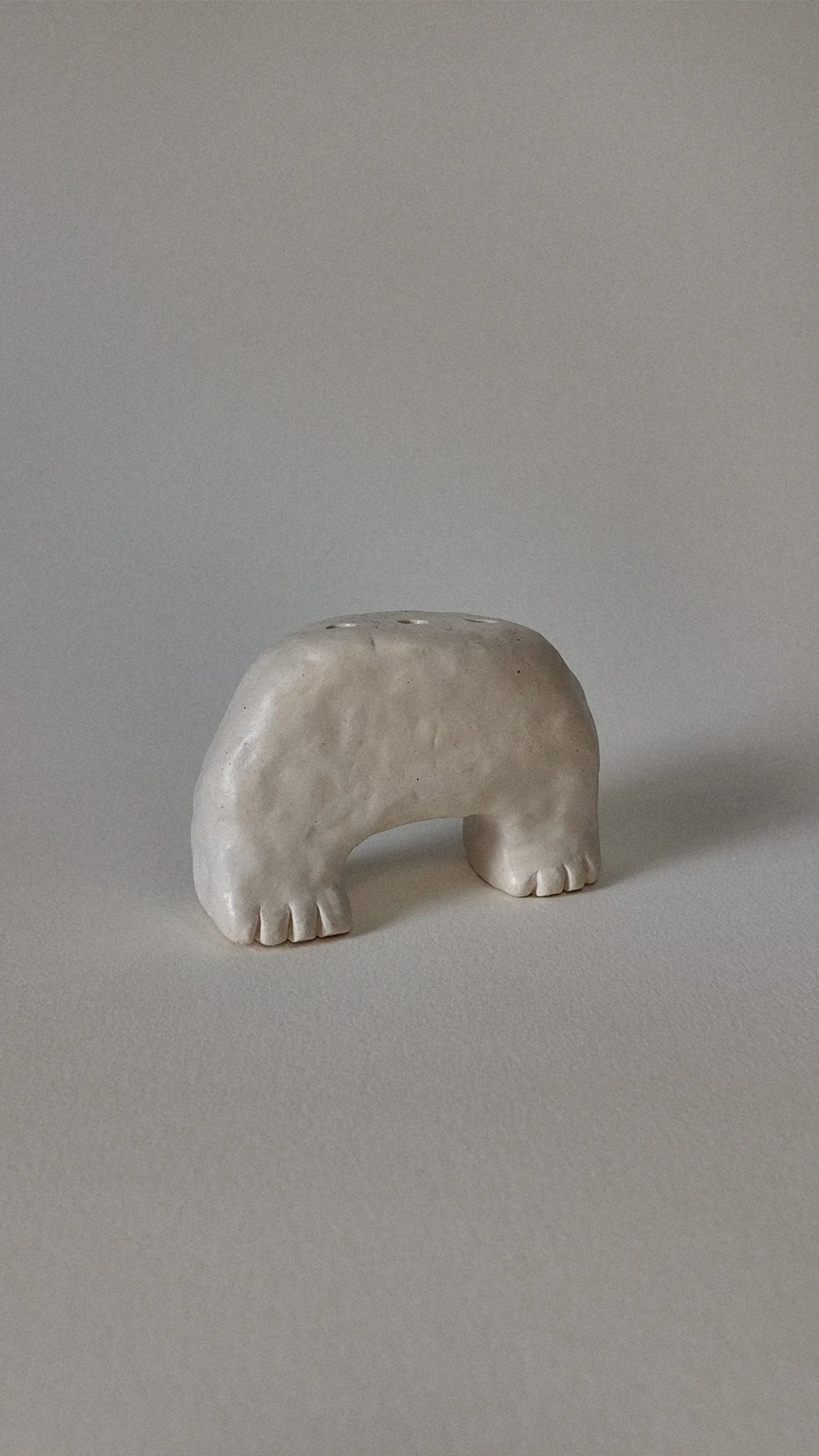 Small sculpture resembling an elephant with a minimalist design, made of a light-colored material, on a plain surface with a neutral background.
