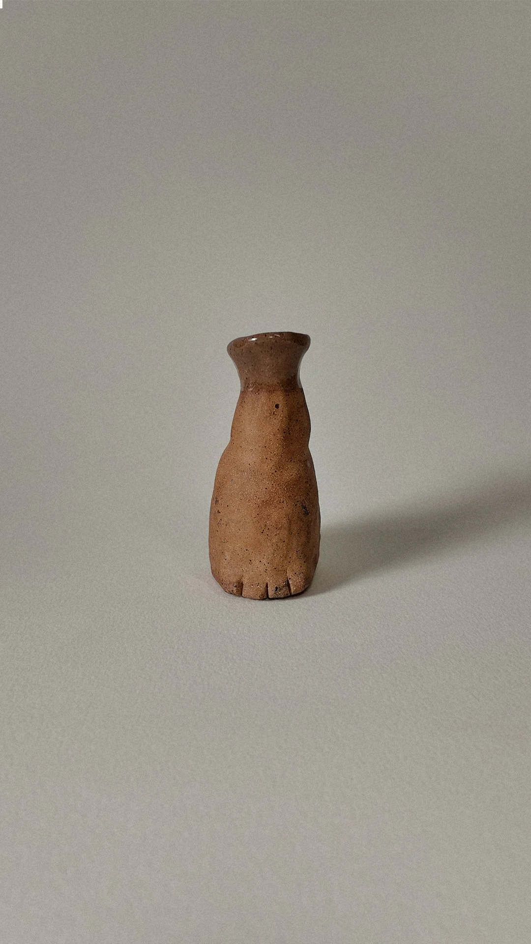 A small, ancient clay figurine resembling a humanoid figure with no detailed facial features, standing upright on a light-colored surface with a plain background.