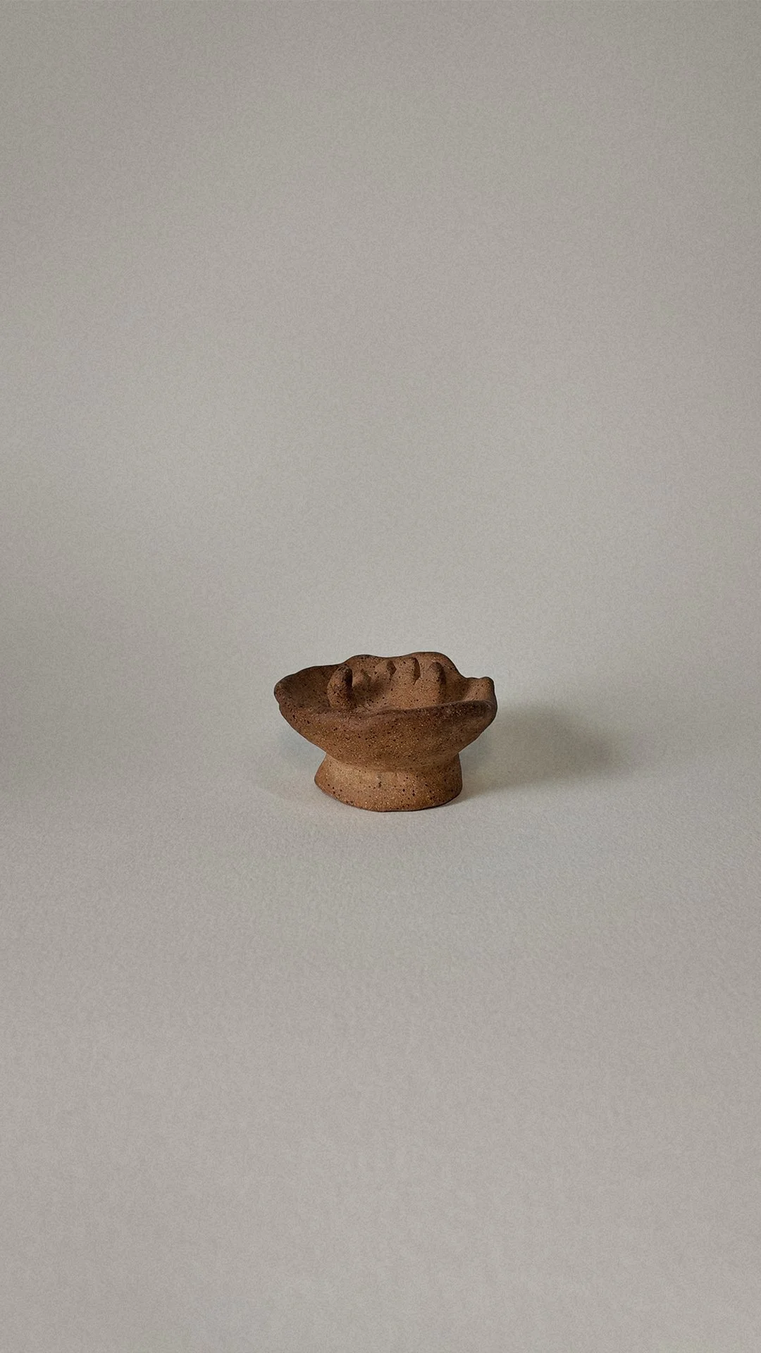 Small ceramic sculpture of a human face, placed on a plain light background.