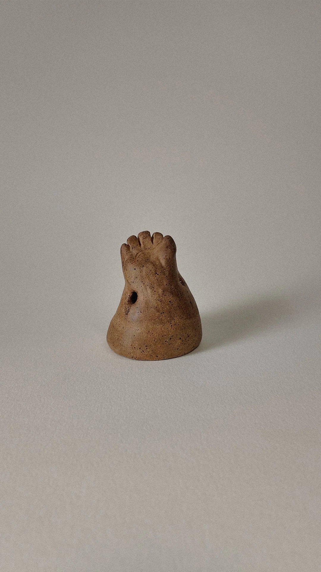 Small ceramic sculpture resembling a bunny with a rough, textured surface, placed on a plain, light-colored background.