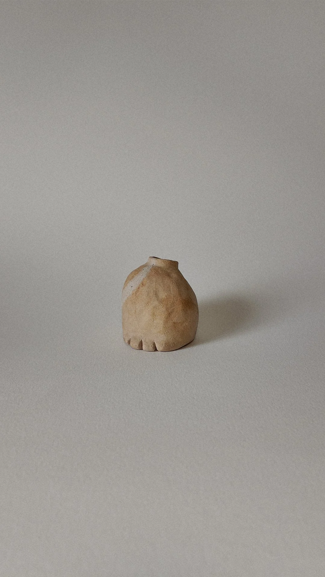 Small beige ceramic vase with a textured surface and scalloped base, placed on a plain light-colored surface