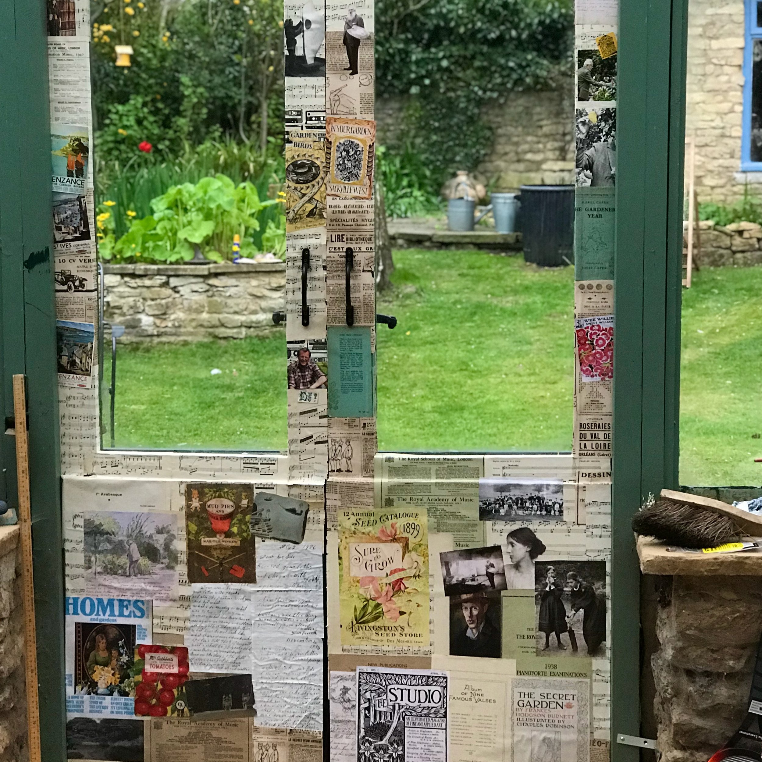 A collage of vintage papers, posters, and photographs attached to a frame, with a garden in the background.
