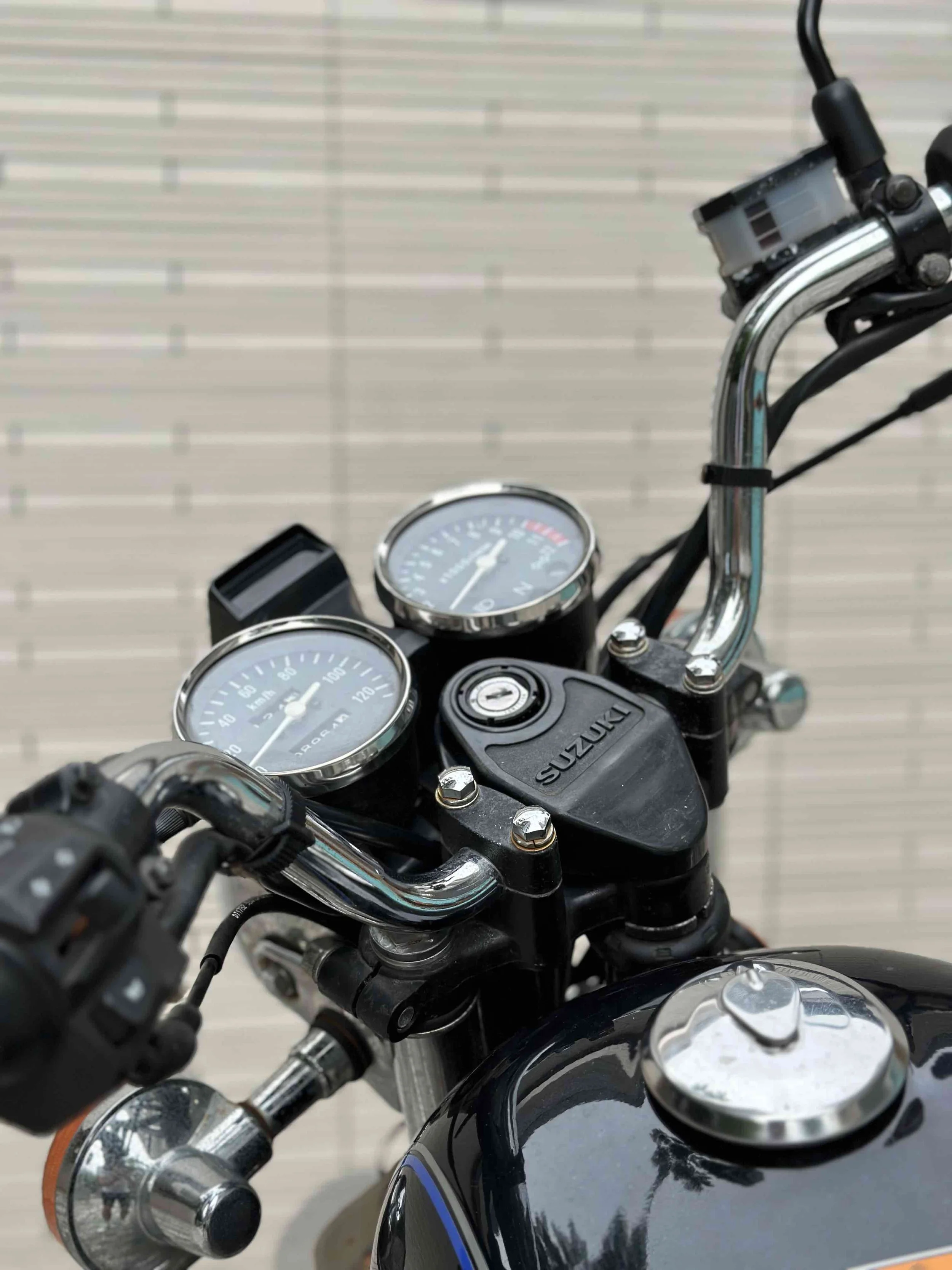 Close-up view of a Suzuki motorcycle's handlebar, showing gauges, ignition, and chrome parts.