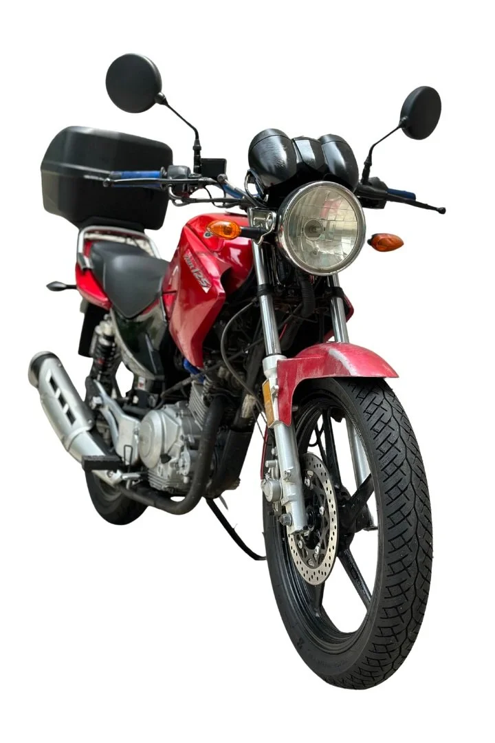 Red and black motorcycle with a black top case, round headlight, and front disc brake.