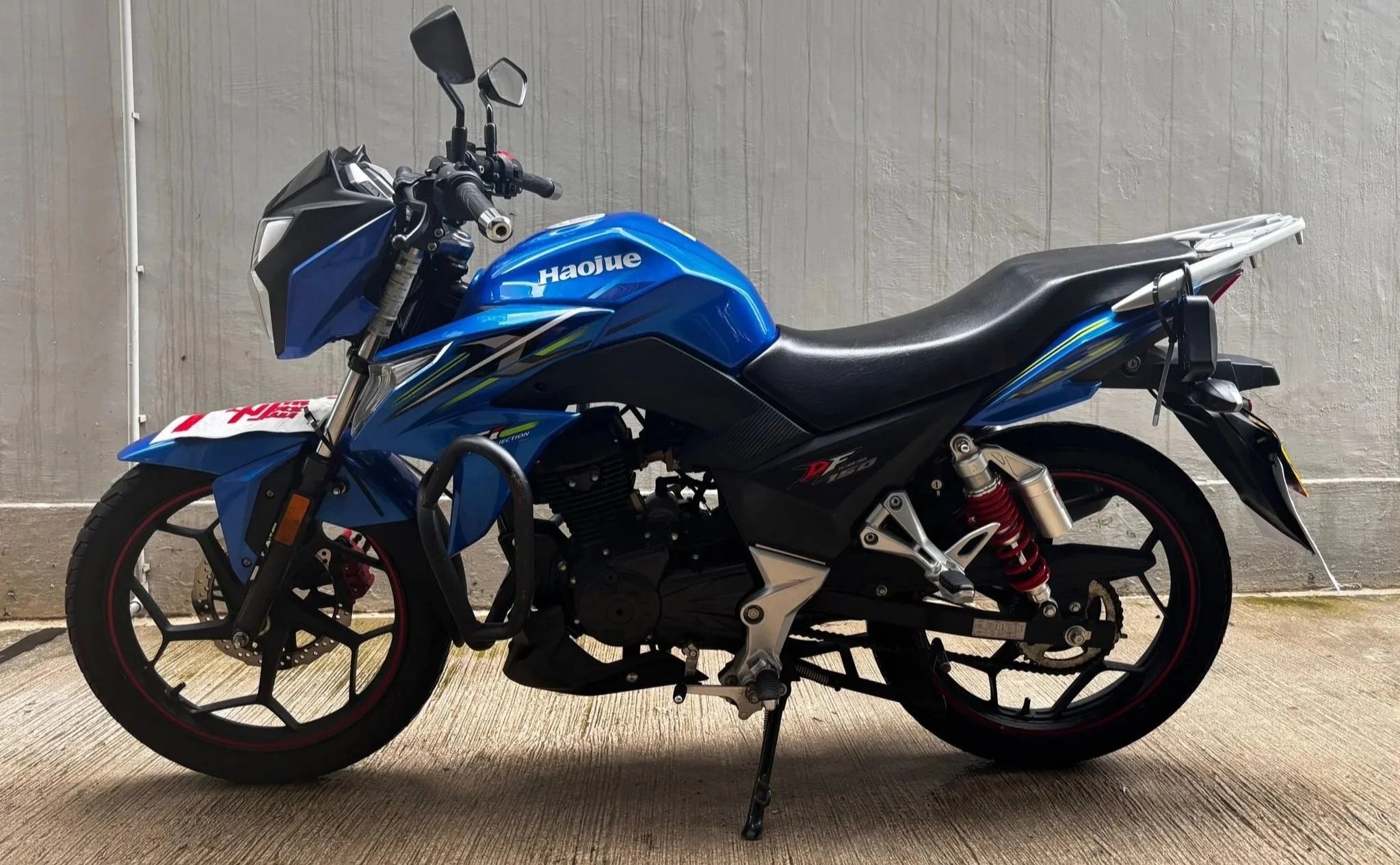 A blue and black sport motorcycle parked on a concrete surface next to a plain light-colored wall.
