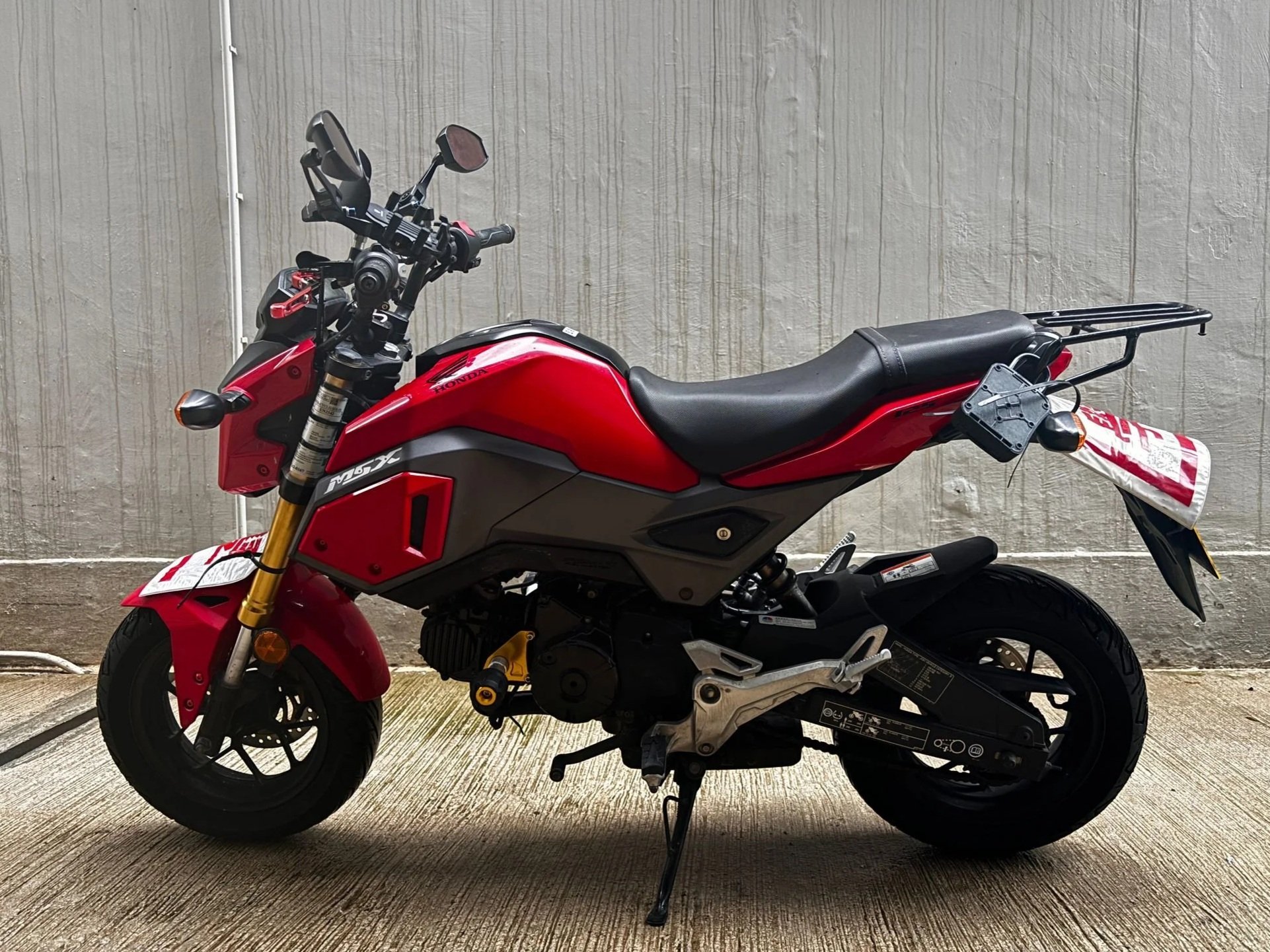 Red and black Honda motorcycle parked on a concrete surface against a textured grey wall.
