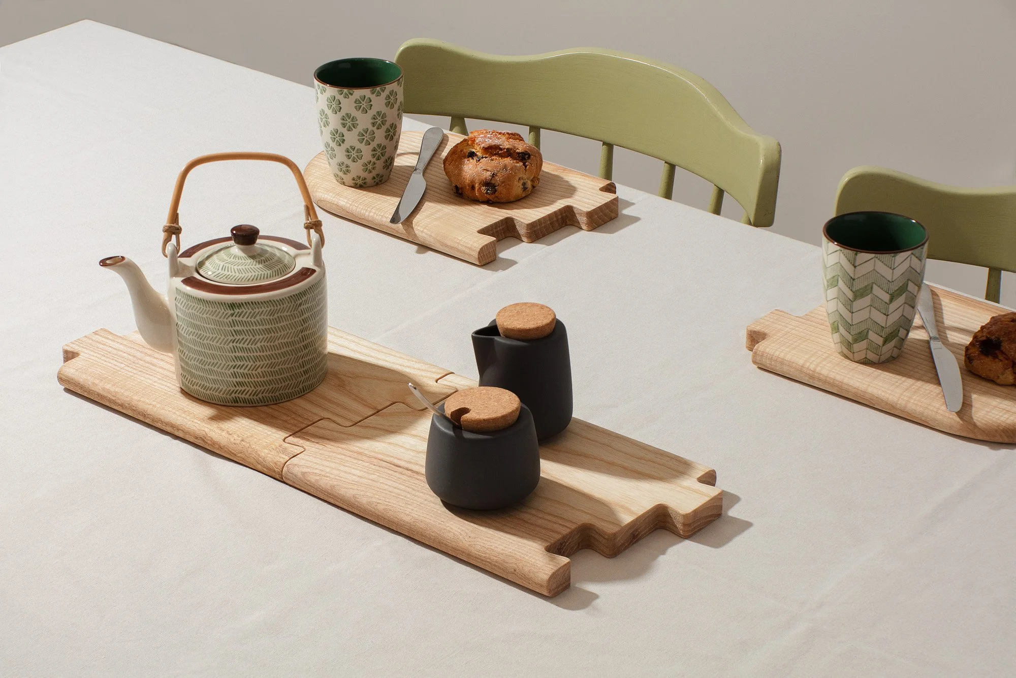Tea set on a dining table with a teapot, cups, mugs, bread boards, and pastries.